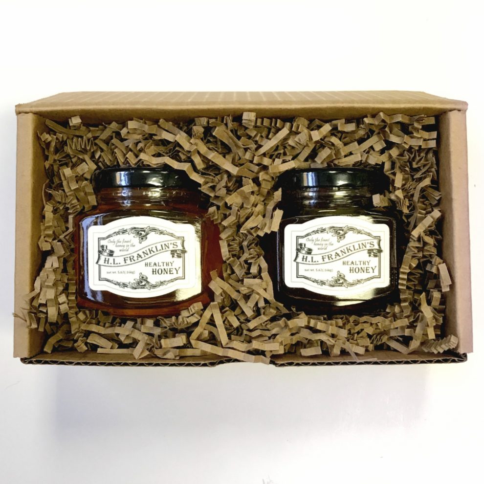 Two jars of preserves in a rustic gift box with decorative shredded paper.