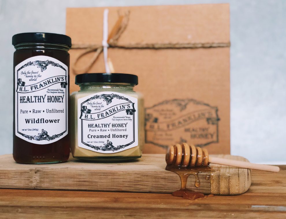 Two jars of honey and a honey dipper on a wooden surface.