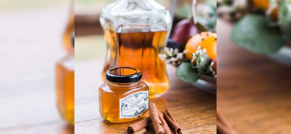 Honey jars and cinnamon sticks on a wooden table with flowers.